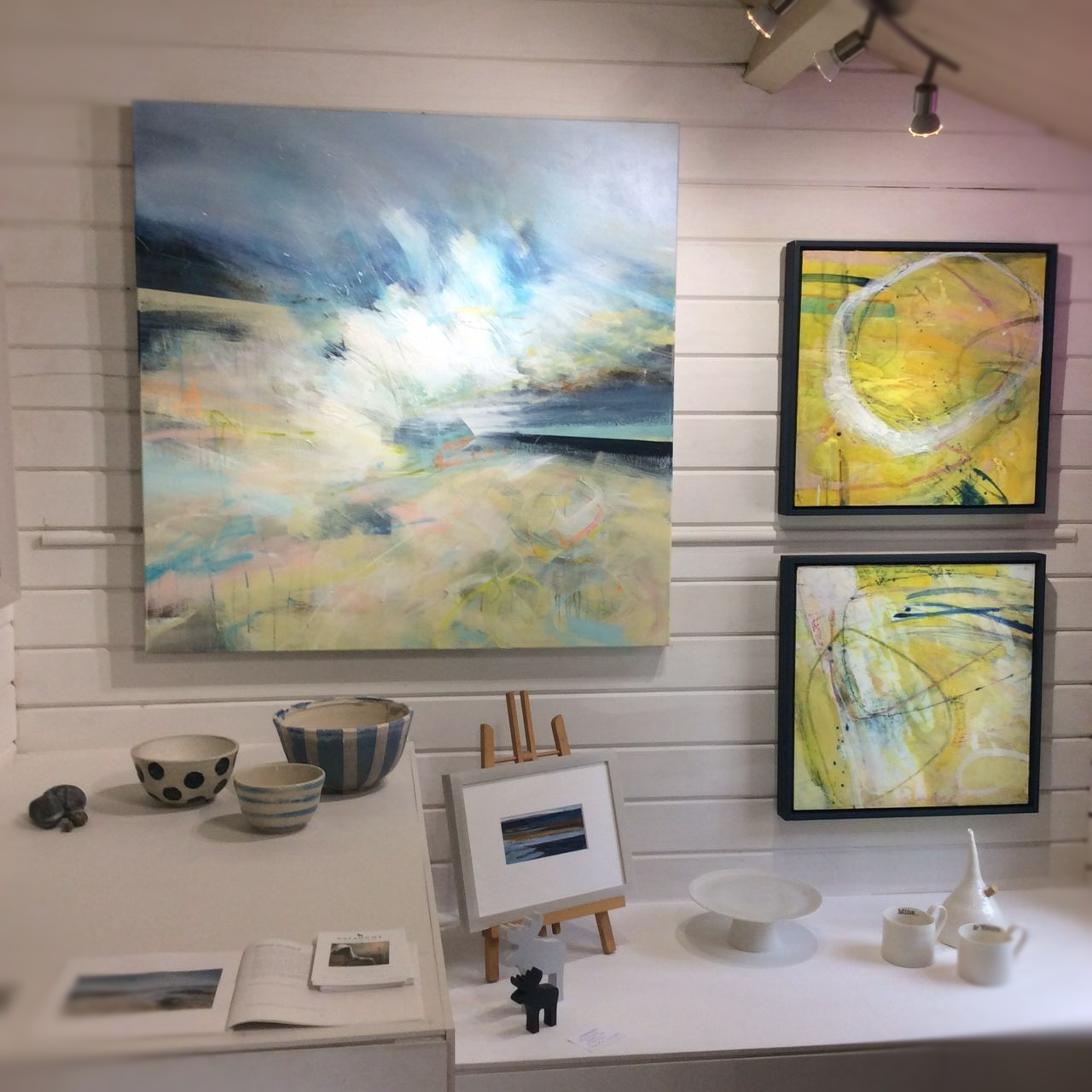 gallery wall with yellow abstract encaustic paintings and large seascape