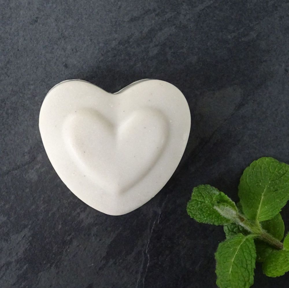 Pale grey heart shaped handmade soap laid flat on slate with fresh mint spr