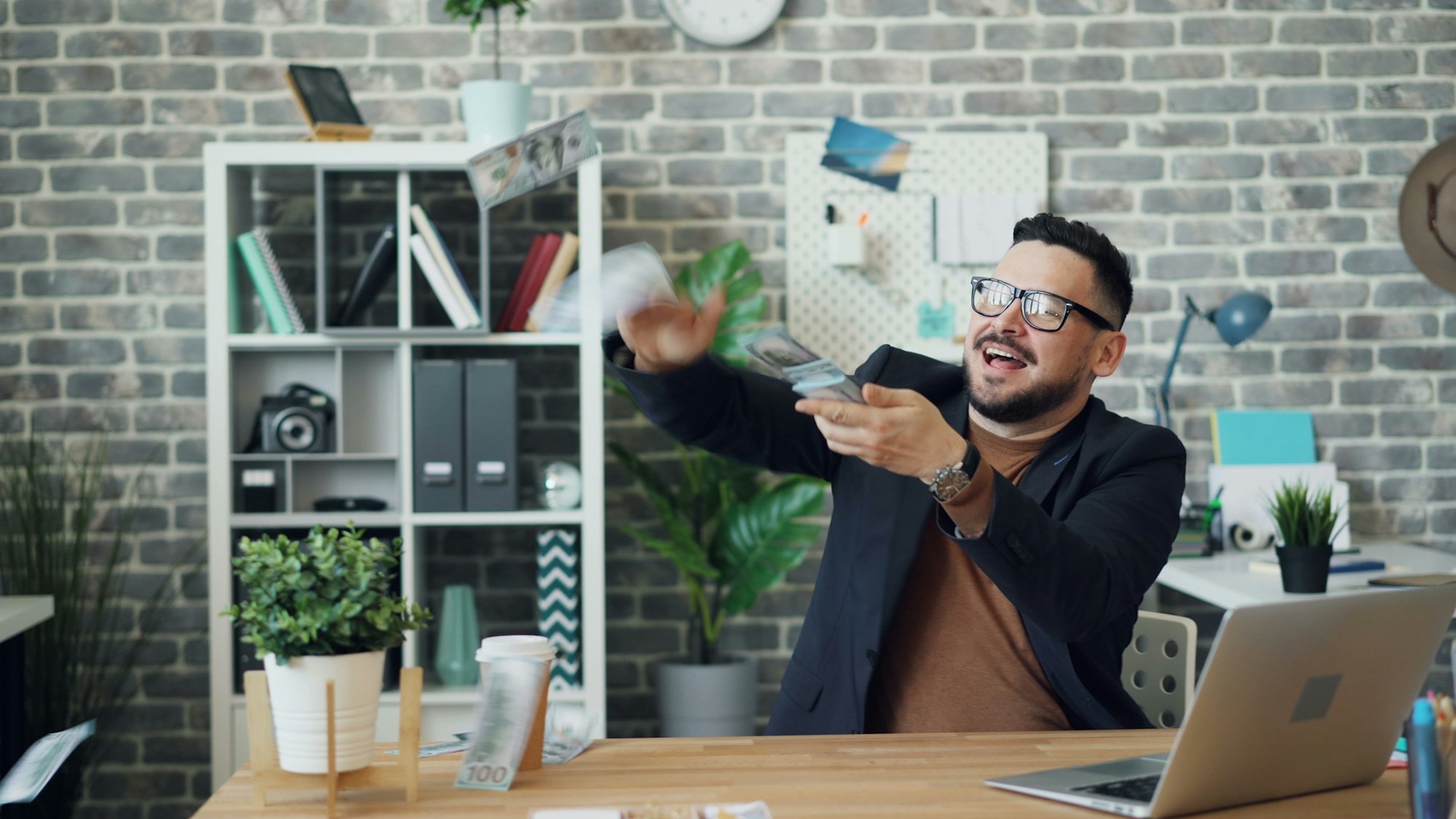 man sitting at desk throwing money into the air