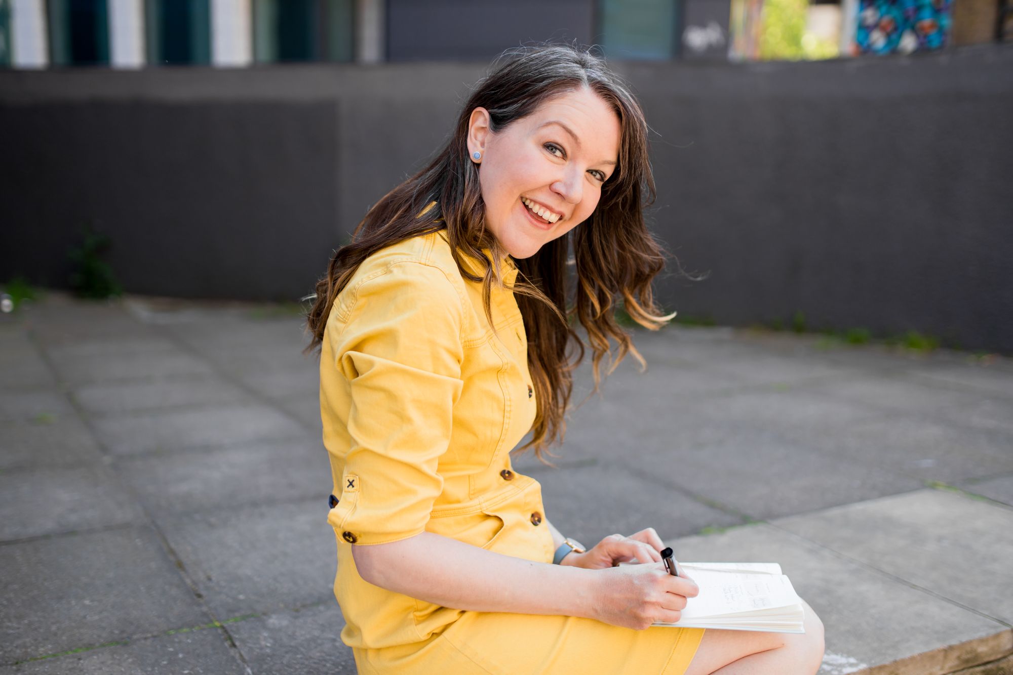 Brighton headshot photographer Lauren Psyk sitting down in the street writing with a pen and notebook