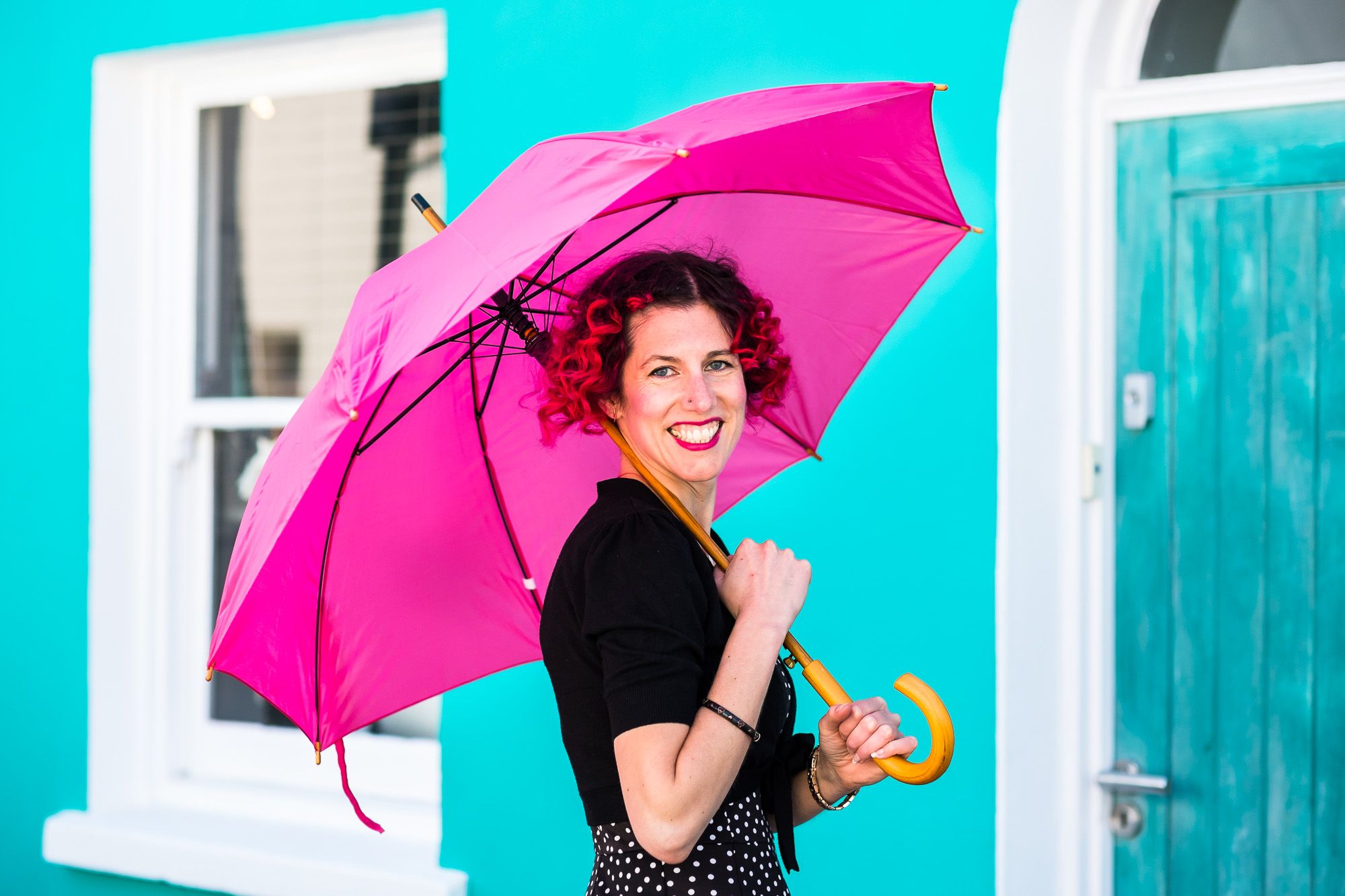 Lady standing in front of a blue wall in Brighton with a pink umbrella