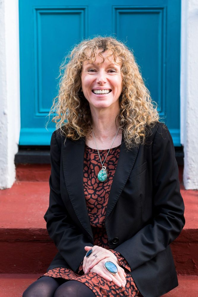 Woman sitting in front of a blue door in Brighton smiling and looking at the camera