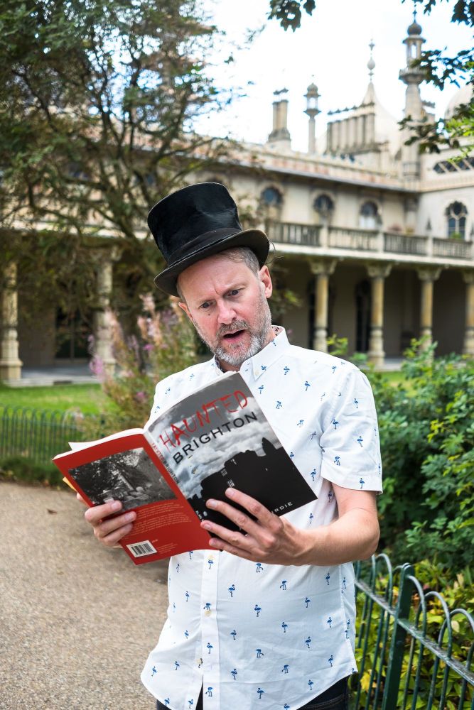A man in a top hat holding a book in Pavilion Gardens in Brighton
