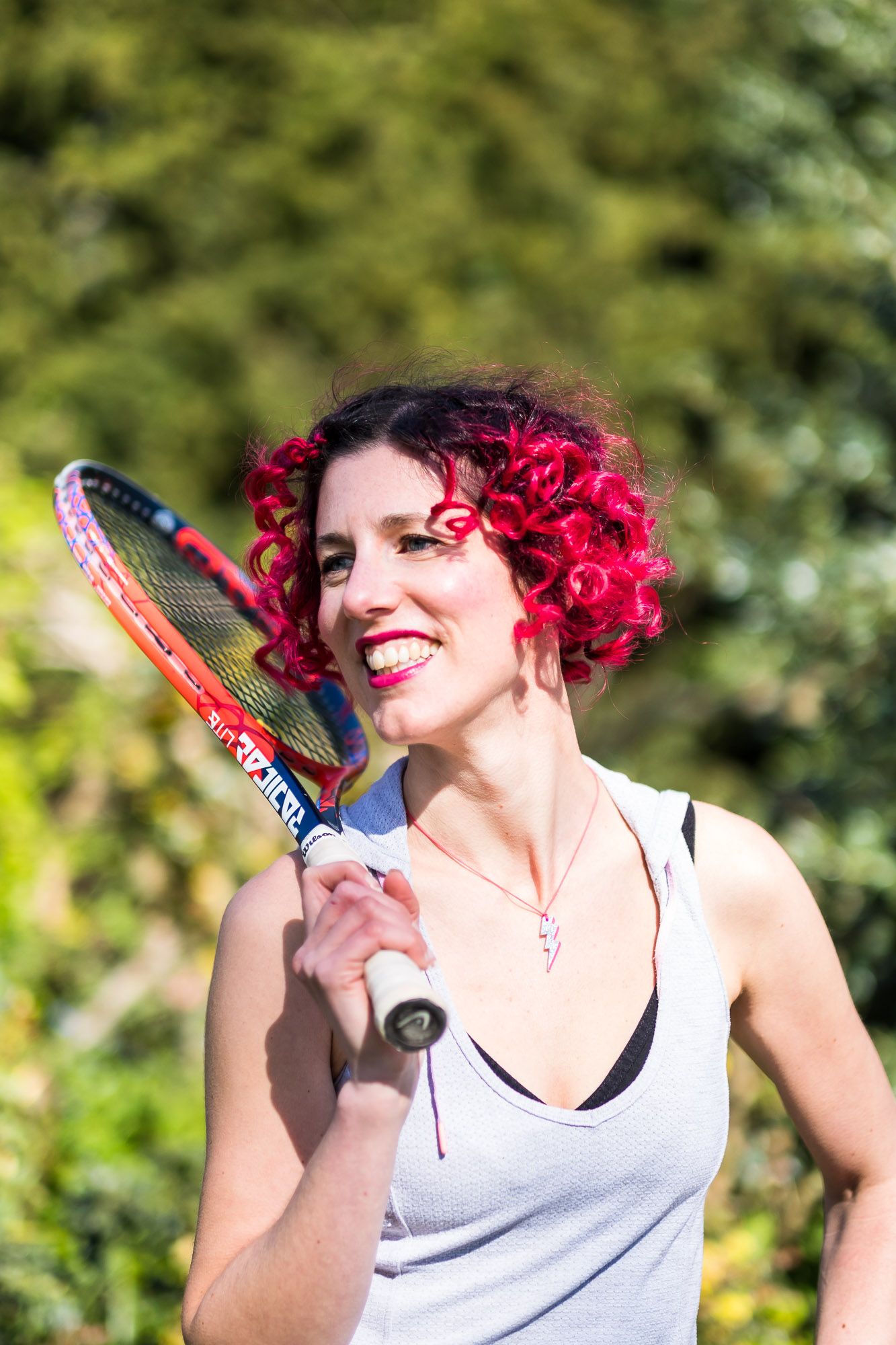 Health coach Lauren Stoney holding a tennis racket and smiling in Pavilion Gardens in Brighton