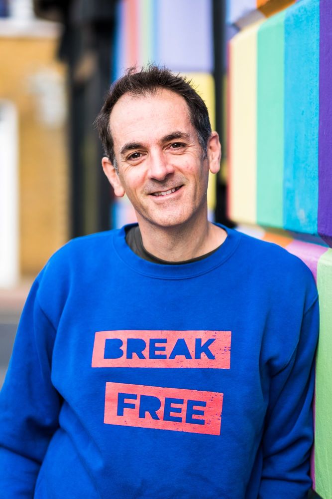 Man leaning against a brightly coloured wall in Brighton wearing a blue sweater