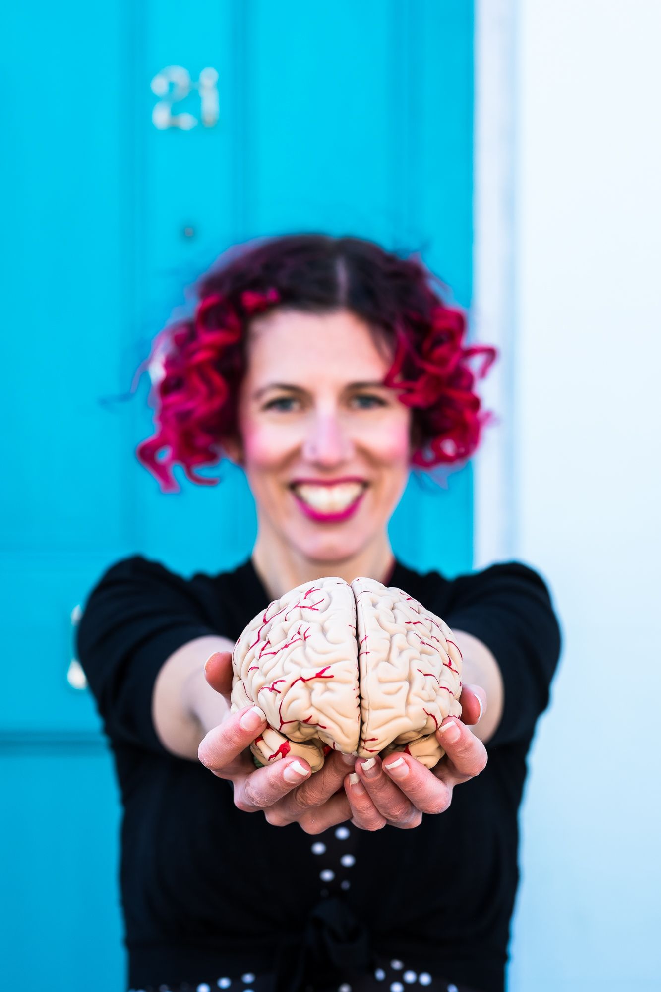 Health coach Lauren Stoney holding a plastic model of a brain and standing in front of a blue door in Brighton