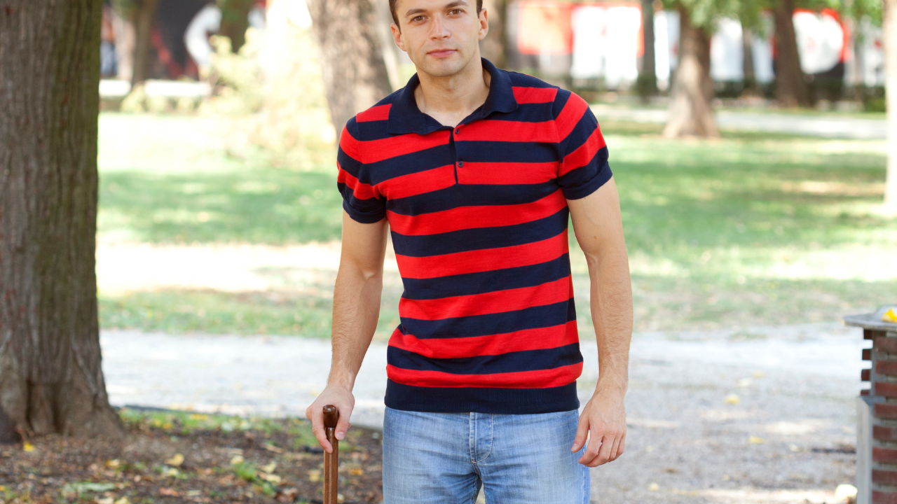 a man with a stripey shirt is holding a walking stick