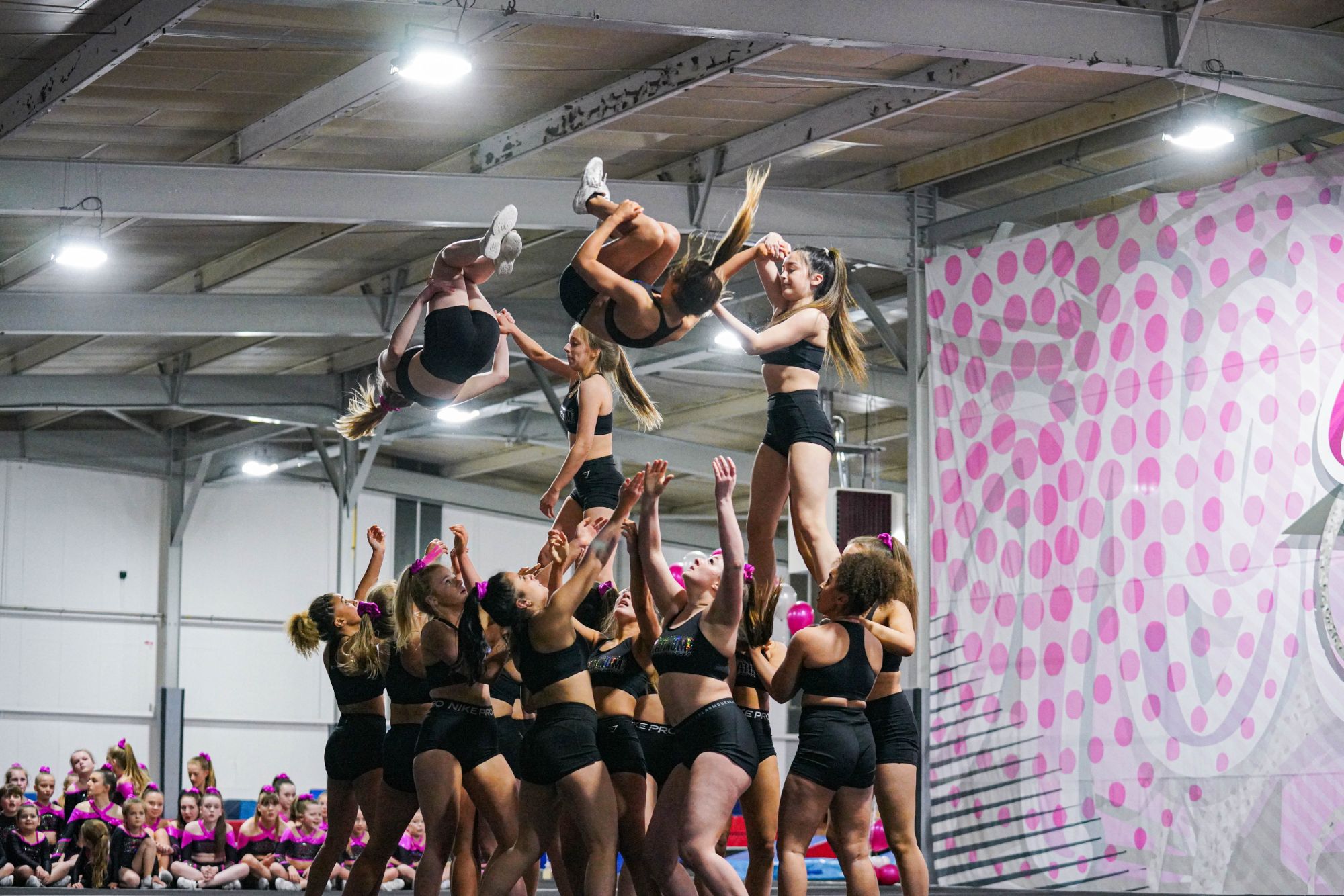 A group of girls doing cheer, with two raised up and standing and two in the air.