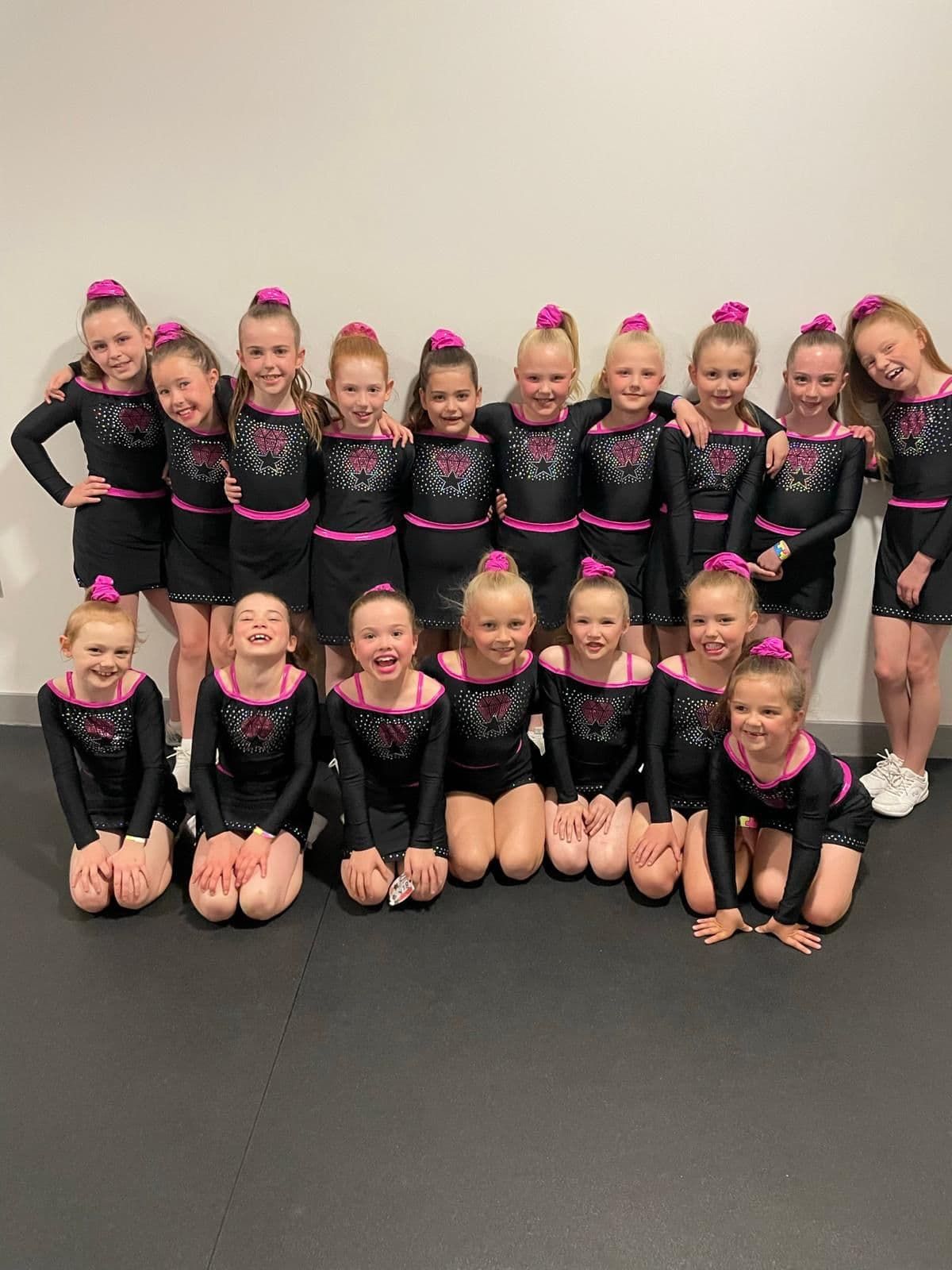 A group photo of young girls in cheer outfits all smiling.