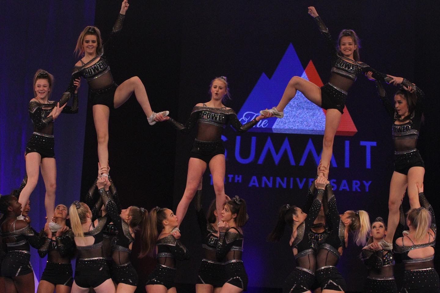 Multiple girls doing cheer, where five girls are held up  in a position by the others.