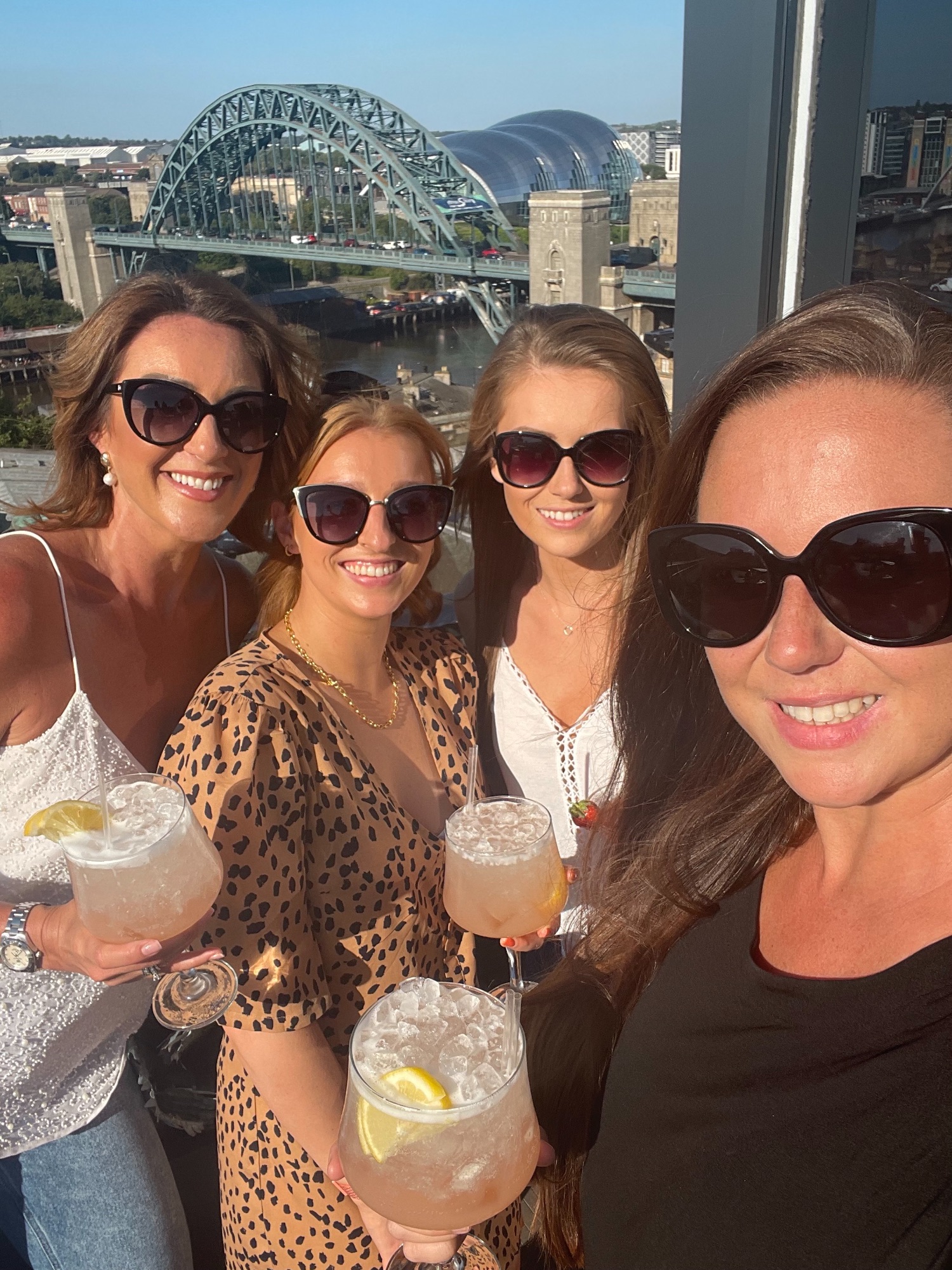 Four women smiling outside with drinks in hand.