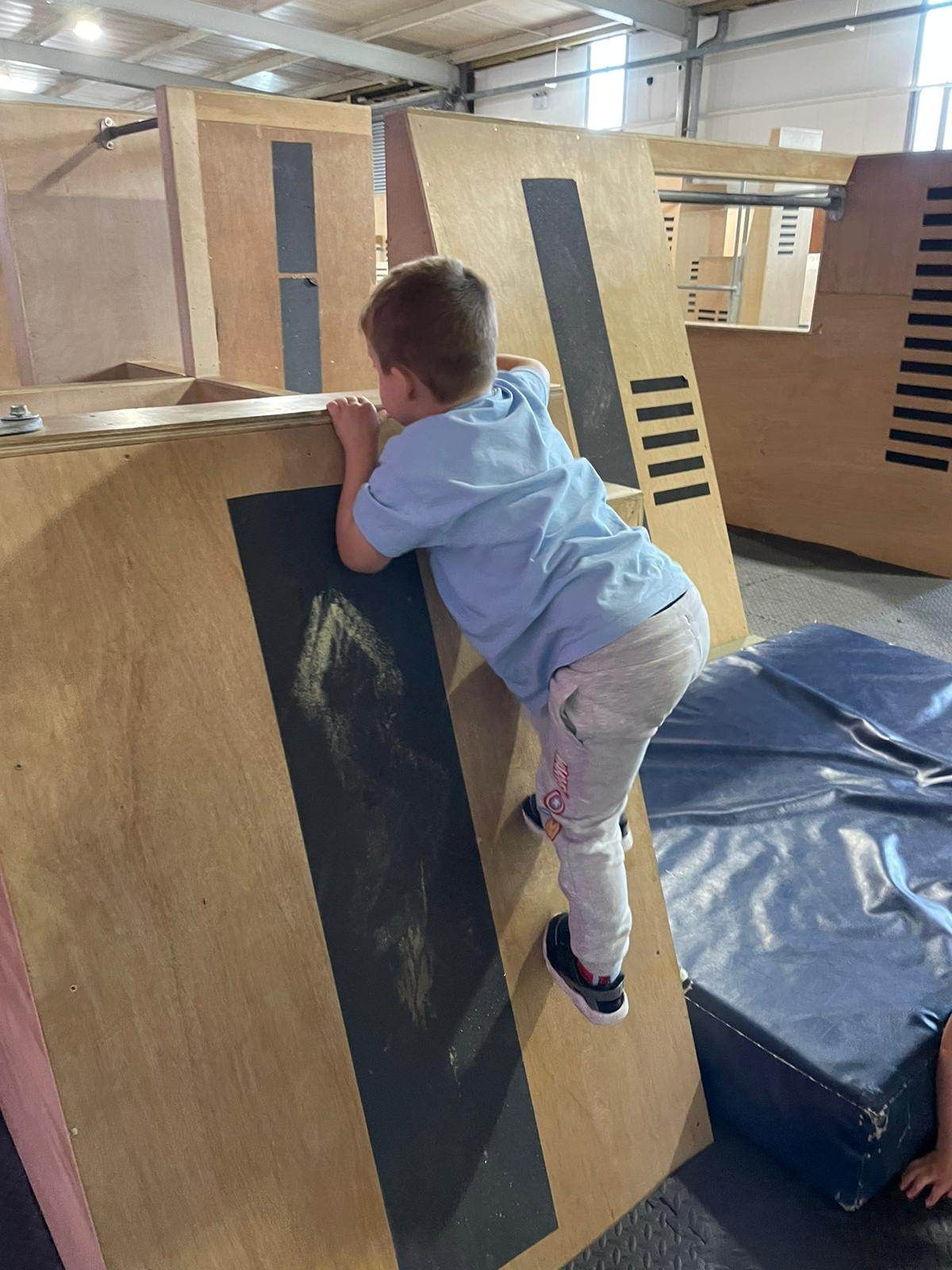 A boy climbing up the side of a piece of wooden eqipment.