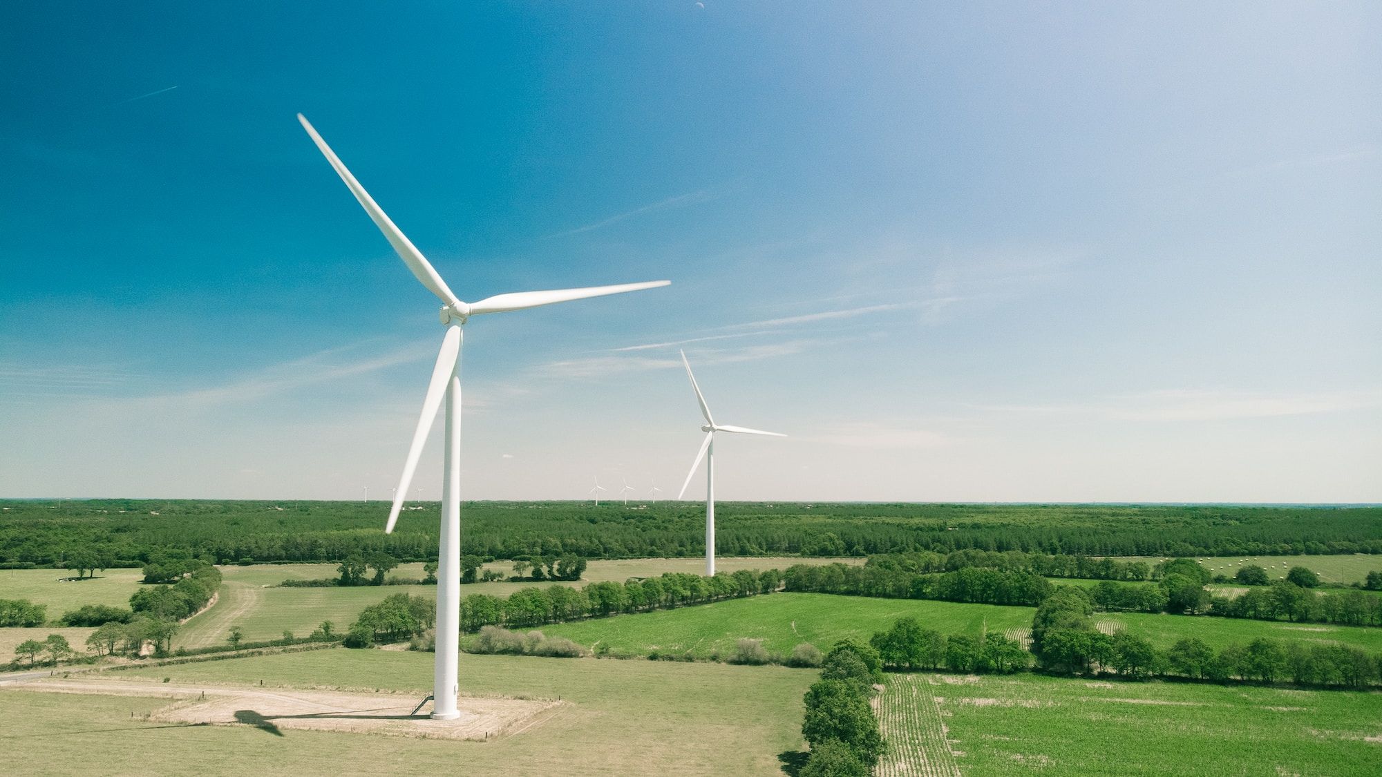 Two wind turbines in green fields with blue sky