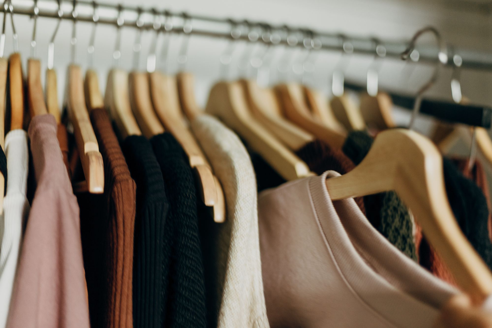 Several neutral coloured tops on clothes hangers on a metal rail , with a beige sweatshirt being selected