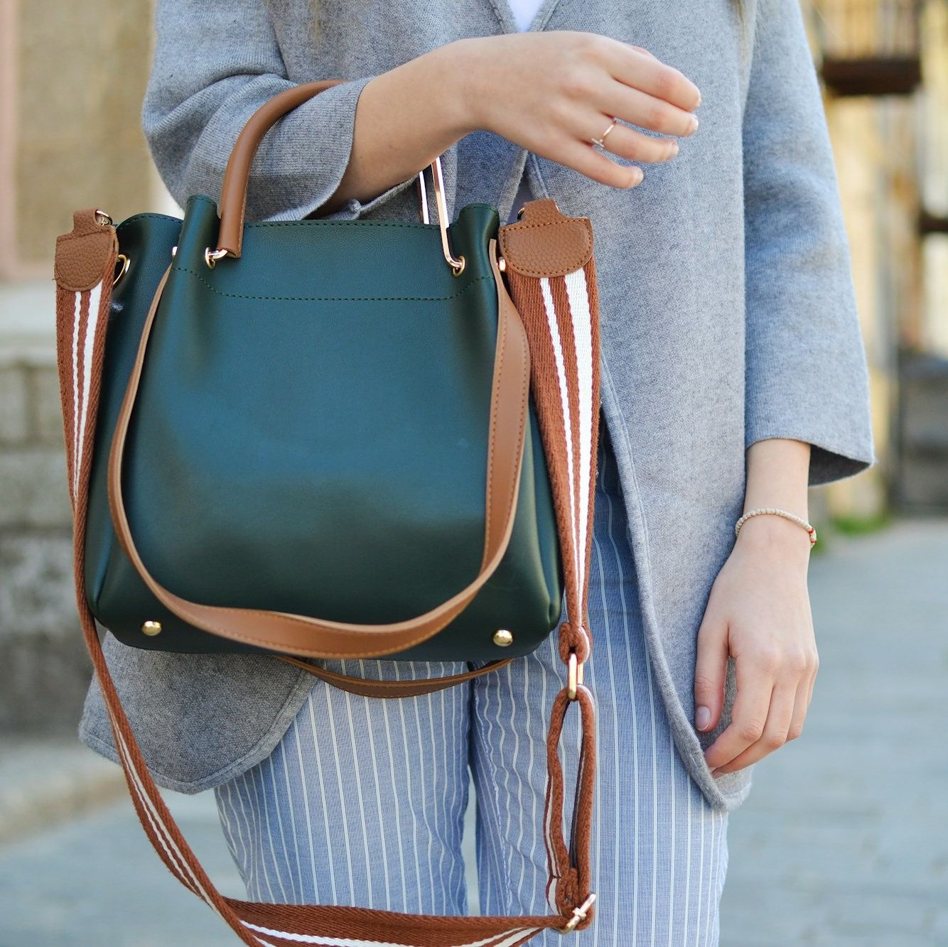 Close up of woman in grey blazer and grey striped trousers, cropped close up on her arm holding a green leather handbag with tan straps