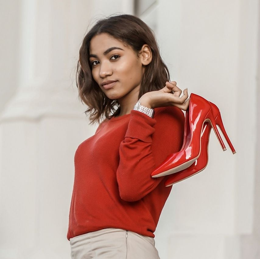 Dark skinned woman in red sweater with red heels held over her shoulder