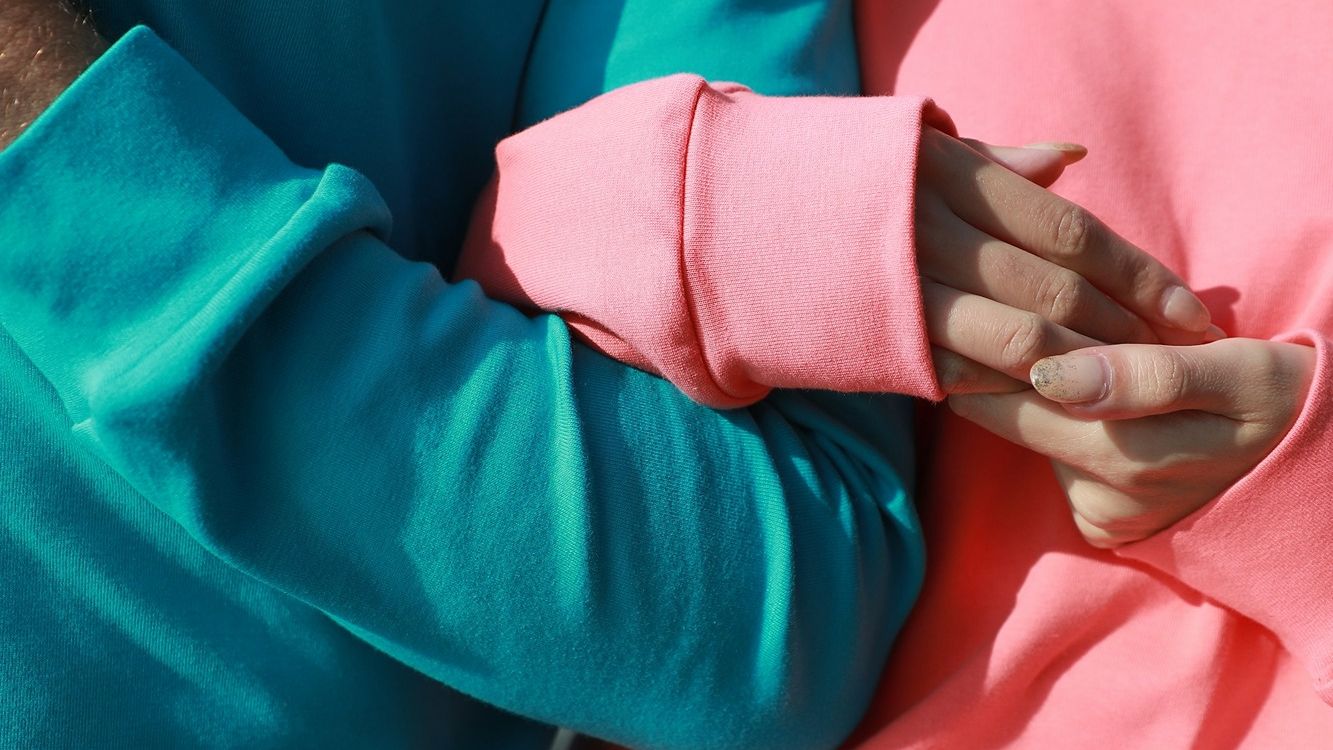 person in blue jumper intertwining arms with person in pink jumper