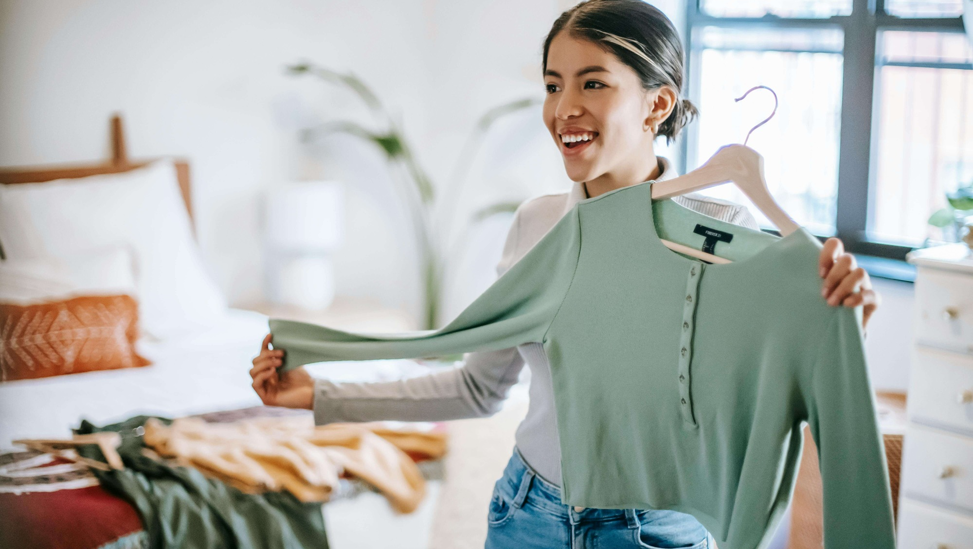 Woman choosing what to wear holding green cardigan up and wearing jeans