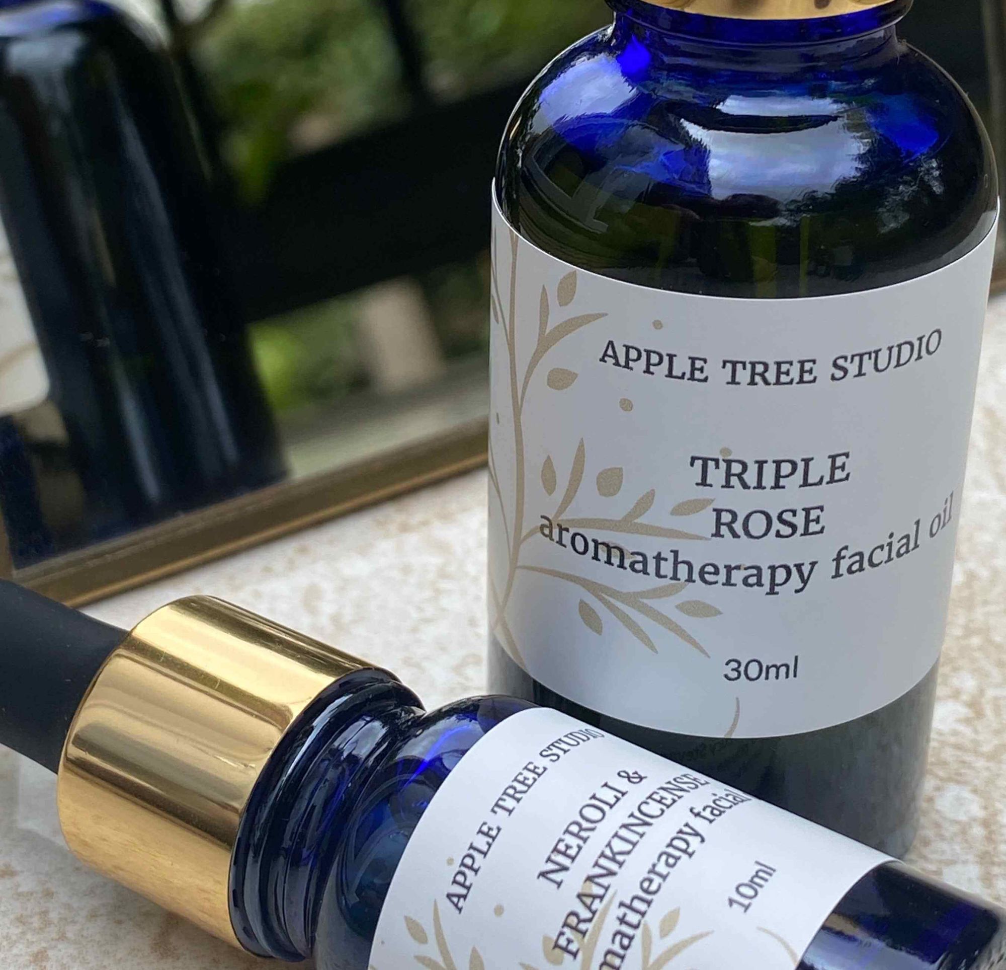 Apple Tree Studio facial oils in blue bottles, featuring Triple Rose and Neroli & Frankincense blends.
