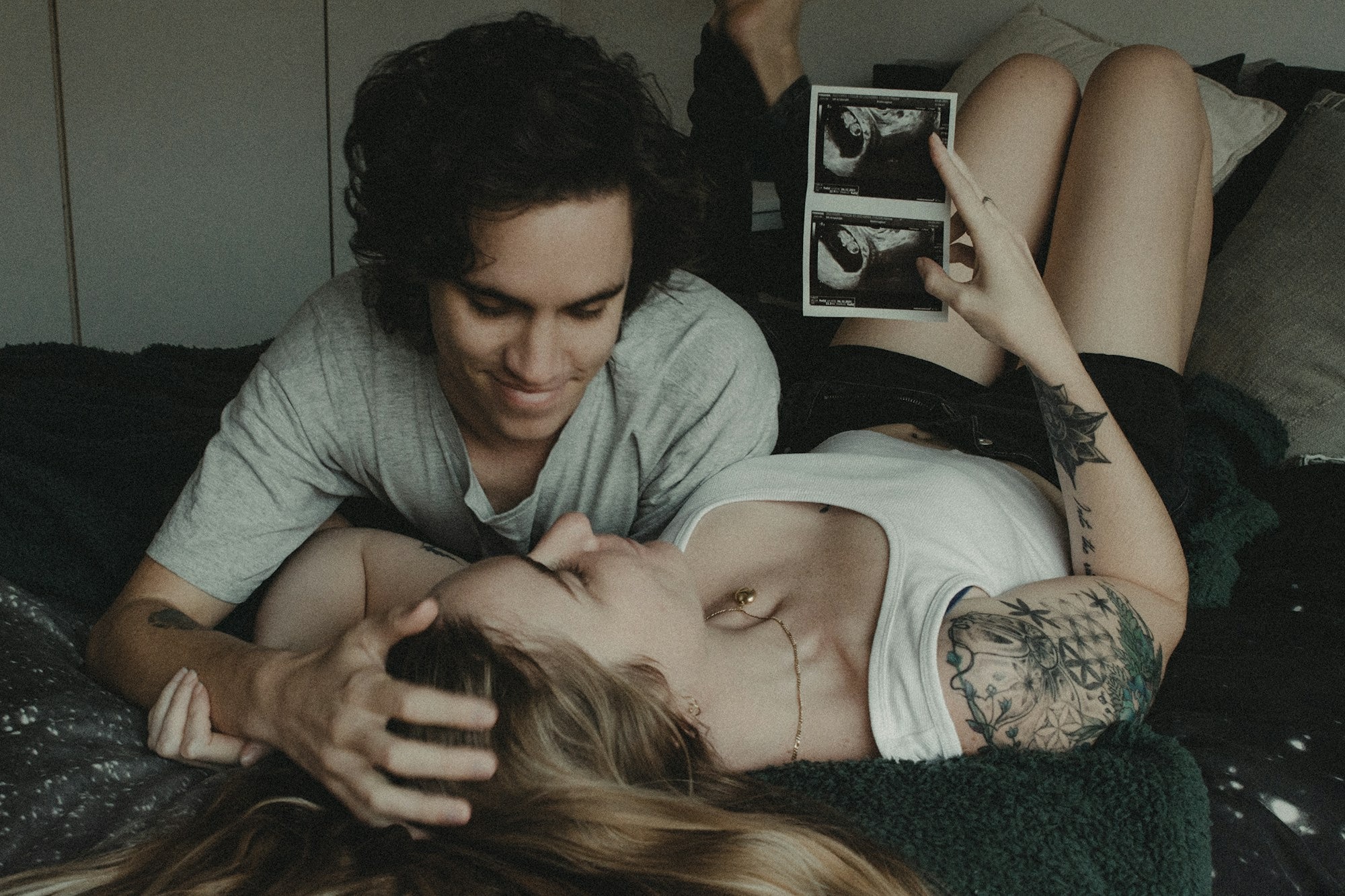 A couple laying down during their pregnancy looking at scan photos of their baby.