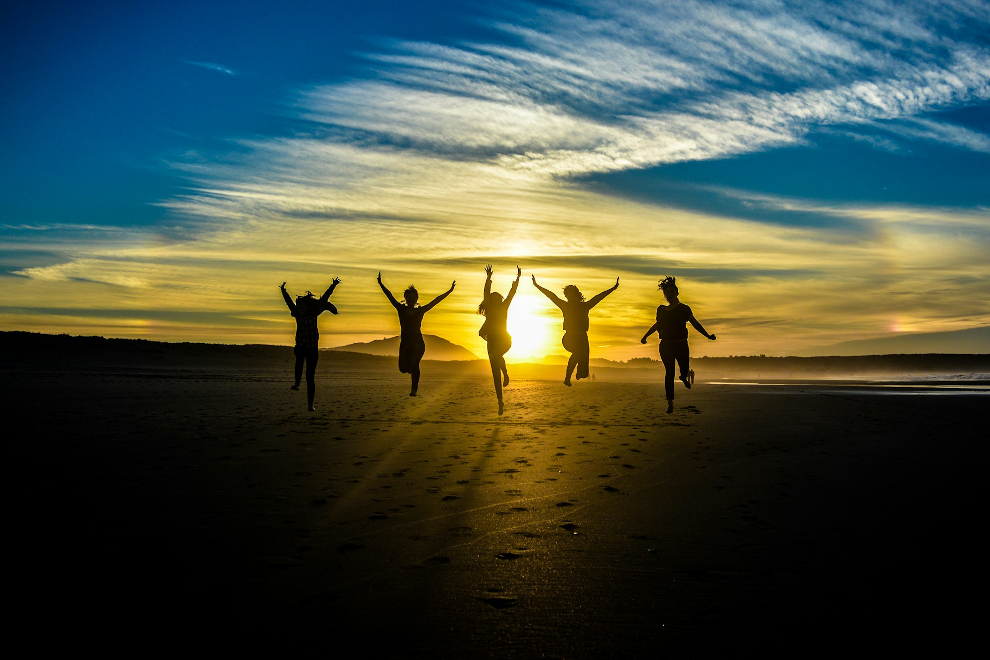 Silhouettes of women jumping on a beach with sun and sky