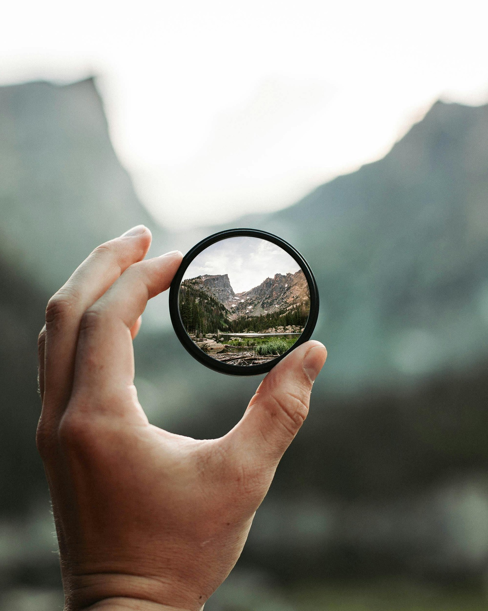 Photo of a hand holding a lens focusing on moutains in the distance.