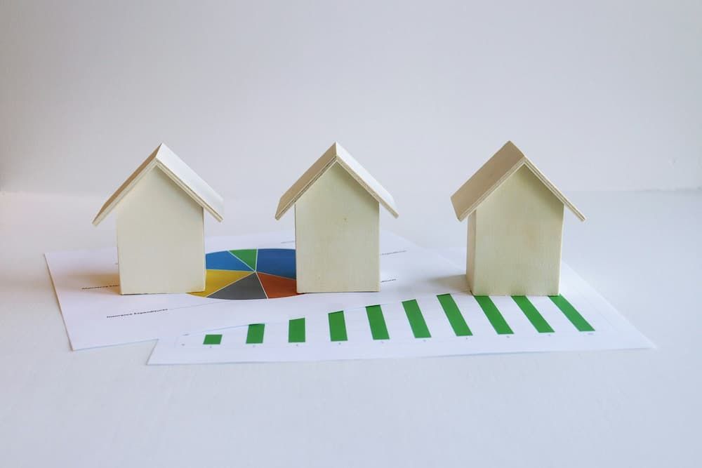three wooden miniature houses in a row on a graph showing increase in value