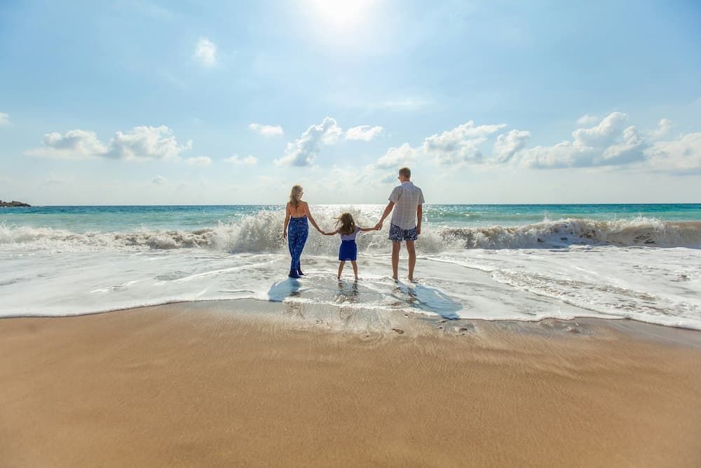 couple with young child on beach letting tide run over their feet on a sunny day