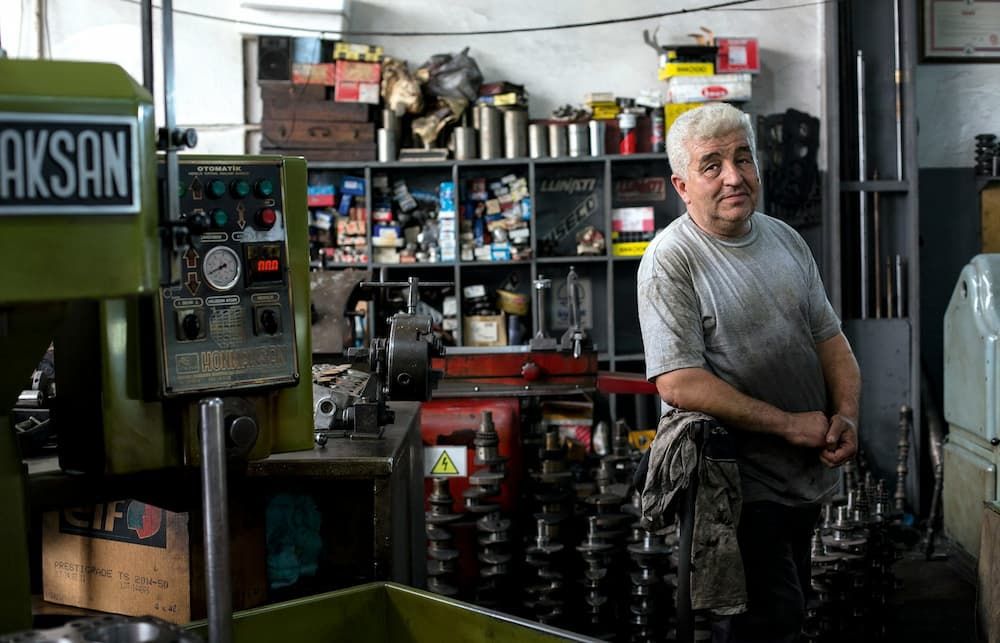 a male mechanic in his 50's with silver hair wearing oily overalls in a workshop