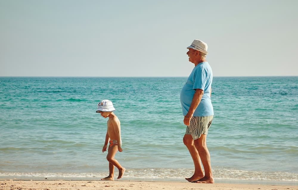 Grandad and Grandchild walking by the sea in sunny weather