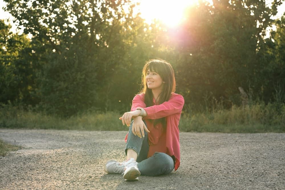 Woman sat on beach looking up at sky smiling