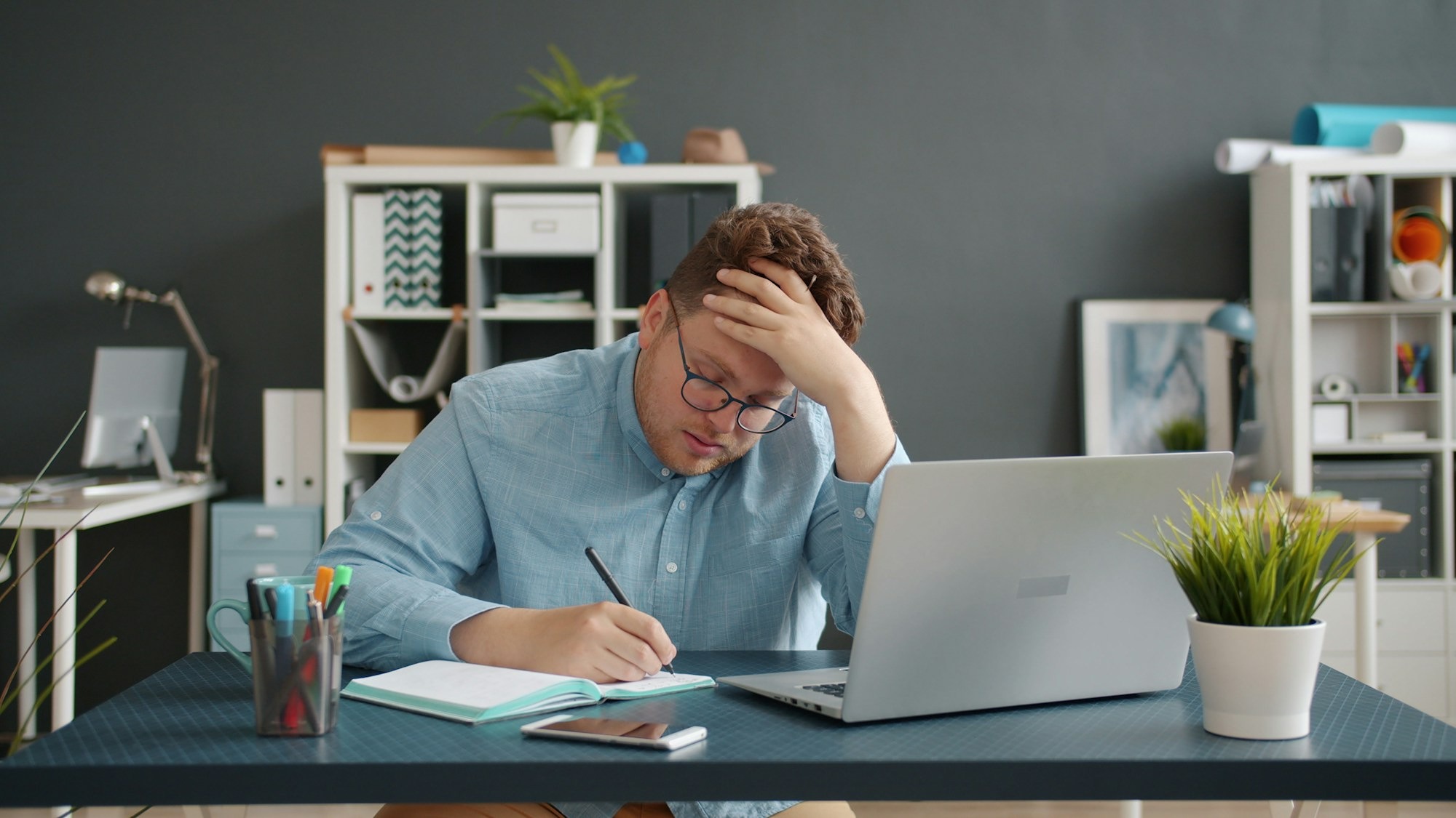 man sitting at his desk, holding his head and looking tired 