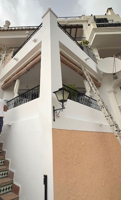 A low-angle shot of a white balcony with a decorative black lantern and a ladder leaning against the wall for renovation work