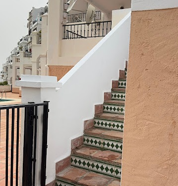 Outdoor tiled stairs with green and white patterned accents leading up a white exterior wall next to a peach-colored textured surface