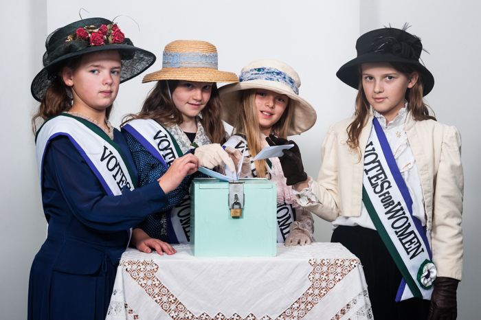 4 female pupils from Patcham Junior School  pose in costume as suffragettes and wearing 'Votes for Women' sashes made in Gladrags sewing workshop.